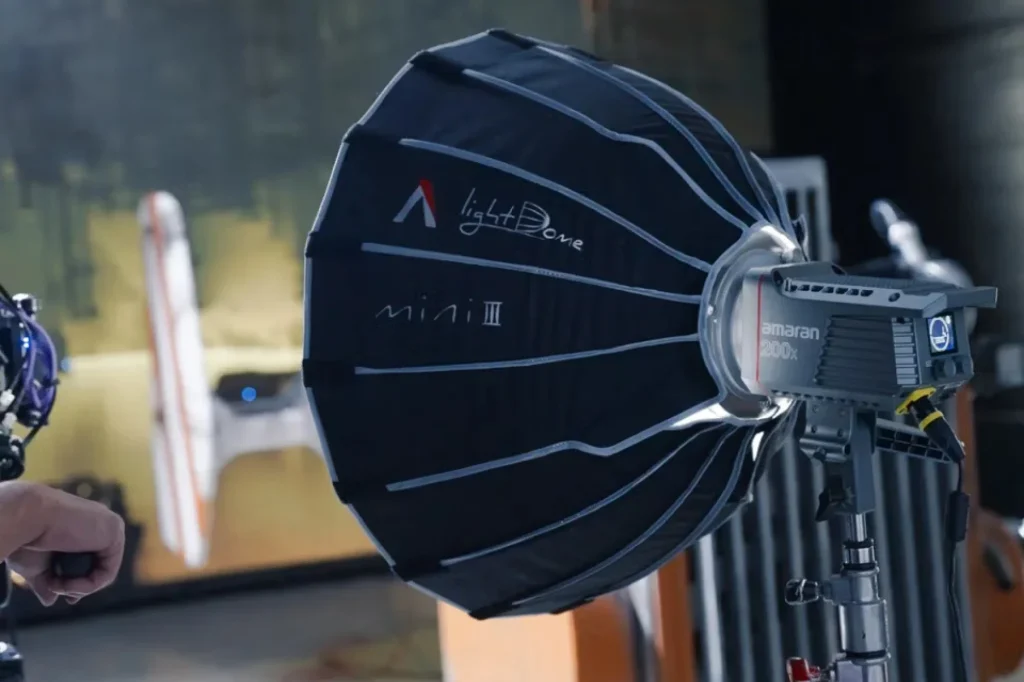 Круглий софтбокс Aputure Light Dome Mini III на прожекторі amaran 200x у студії, видно білий логотип на чорній тканині, рука оператора притримує прилад